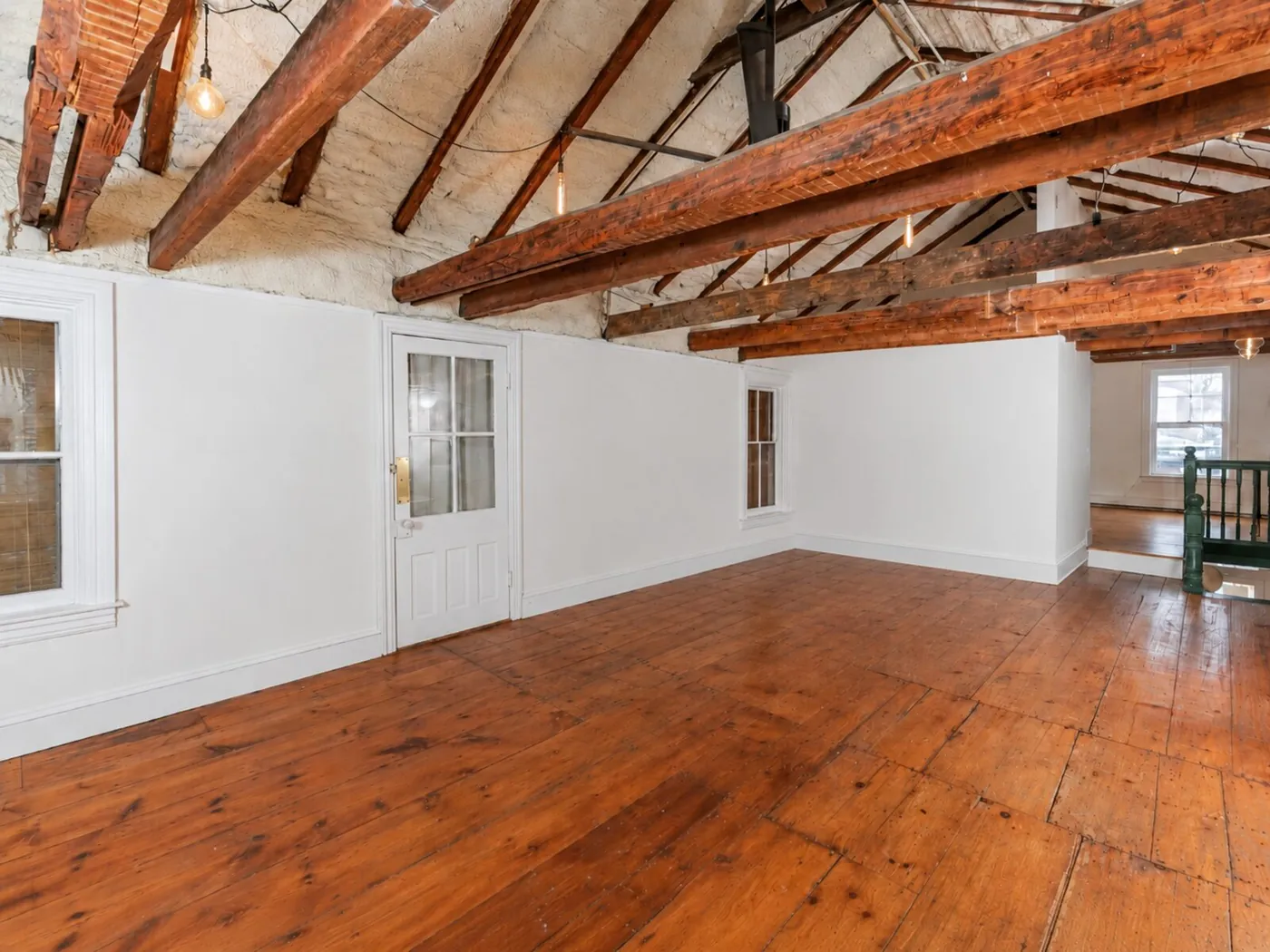 A large open room under a beamed ceiling with a warm pine floor